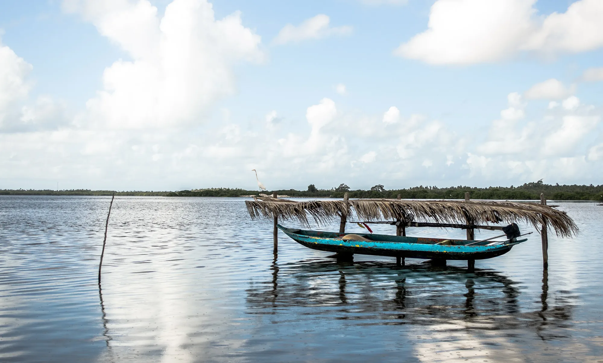 Canoa ancorada nas águas calmas da Lagoa Manguaba, em Marechal Deodoro, sob céu azul com nuvens